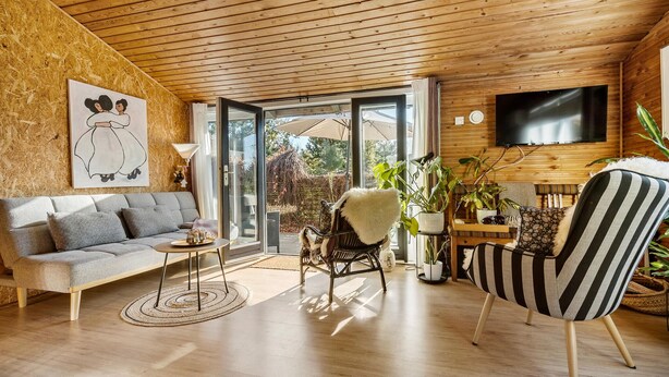 Una sala de estar acogedora con techo de madera, un sofá gris, un sillón a rayas y un televisor montado en la pared.