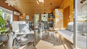 Un acogedor interior de cabaña con techo de madera, una zona de comedor con mesa redonda y un sofá.