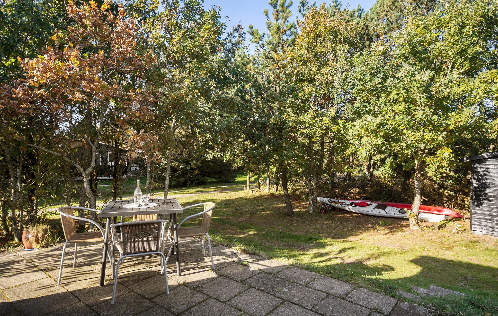 Un patio exterior con una mesa y sillas, rodeado de árboles y un kayak al fondo.