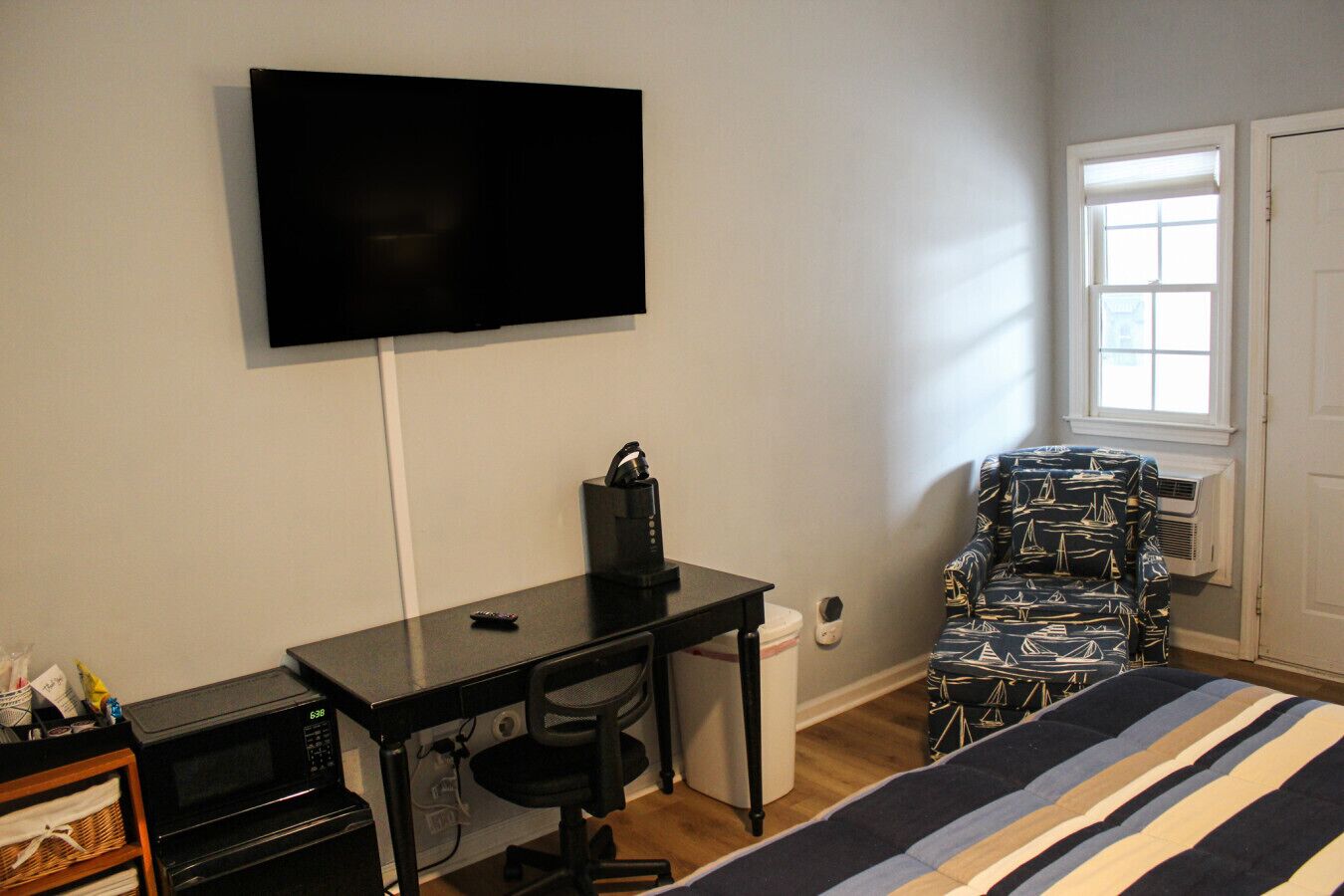 A compact room with a bed, a desk with a chair, a television mounted on the wall, and a window with a view.