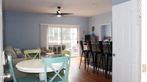 A dining area with a round table and chairs, a ceiling fan, and a view through a glass door to the outside.