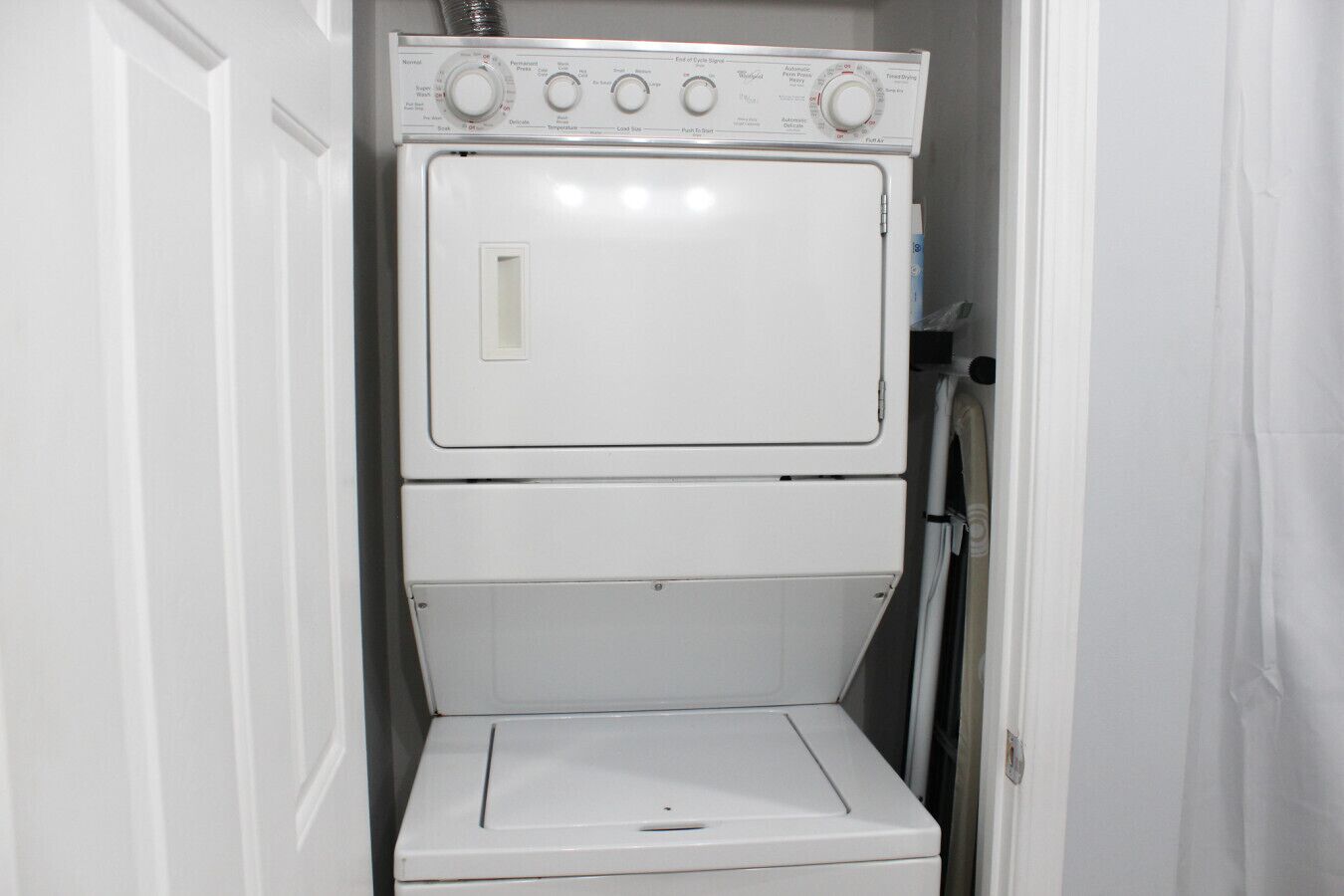 A compact, white laundry room with a stacked washer and dryer, a small window, and a door.
