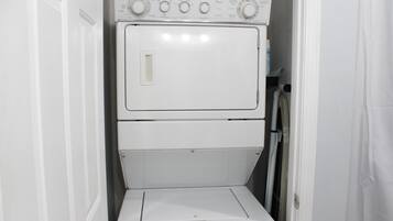 A compact, white laundry room with a stacked washer and dryer, a small window, and a door.