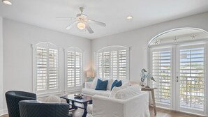 A spacious living room with a white sofa, blue cushions, and a ceiling fan.