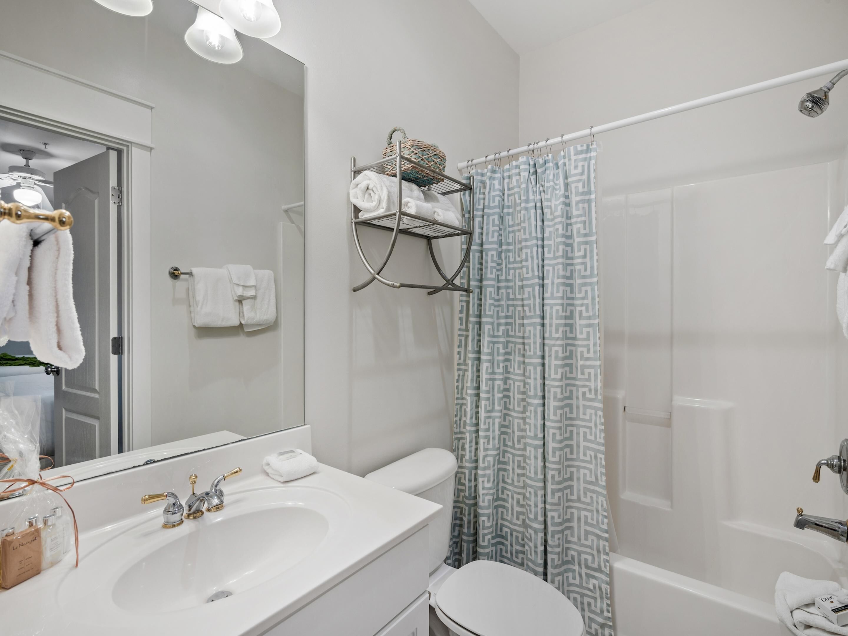 A modern bathroom with a white sink, toilet, and shower. There is a towel rack with towels and a basket with toiletries.