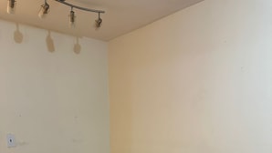 A corner room with a wooden floor, a white ironing board, and a ceiling light fixture.