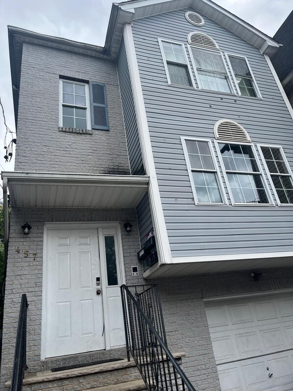 A two-story house with a white front door, a garage door, and a brick foundation. - NWK 457 ROOM 113-C (Newark)