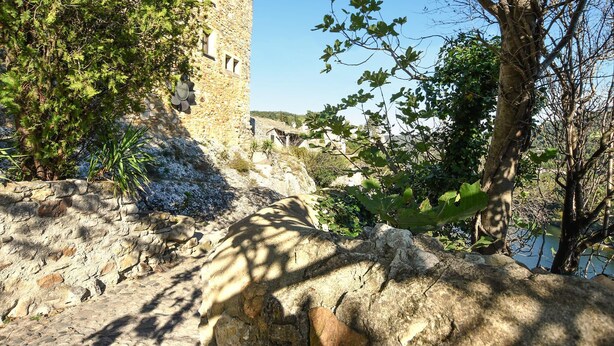 Un edificio de piedra de aspecto rústico, rodeado de árboles y terreno pedregoso.