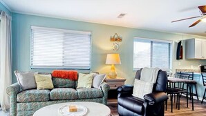 A living room with a patterned sofa, a black leather chair, a white coffee table, and a lamp. - North Myrtle Retreat, 2bd 2ba apartment in 3unit building 1-block from the Beach (North Myrtle Beach)