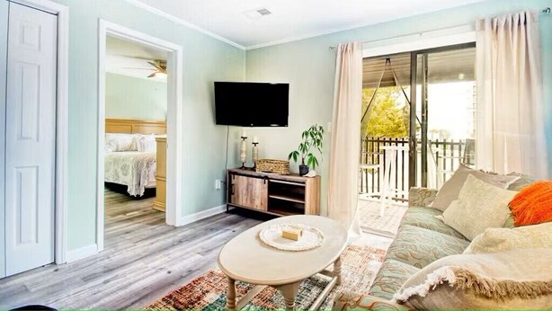 A living room with a sofa, a coffee table, a TV, and a balcony with a view. - North Myrtle Retreat, 2bd 2ba apartment in 3unit building 1-block from the Beach (North Myrtle Beach)