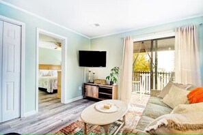 A living room with a sofa, a coffee table, a TV, and a balcony with a view. - North Myrtle Retreat, 2bd 2ba apartment in 3unit building 1-block from the Beach (North Myrtle Beach)
