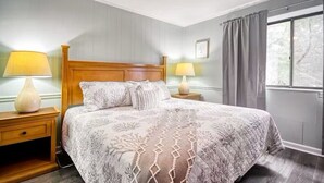A neatly arranged bedroom with a large bed, two bedside tables with lamps, a window with curtains, and a ceiling fan. - North Myrtle Retreat, 2bd 2ba apartment in 3unit building 1-block from the Beach (North Myrtle Beach)