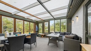 A sunroom with large windows, wicker furniture, and a view of trees. - 2 bedroom amazing home in Kalundborg (Kalundborg)