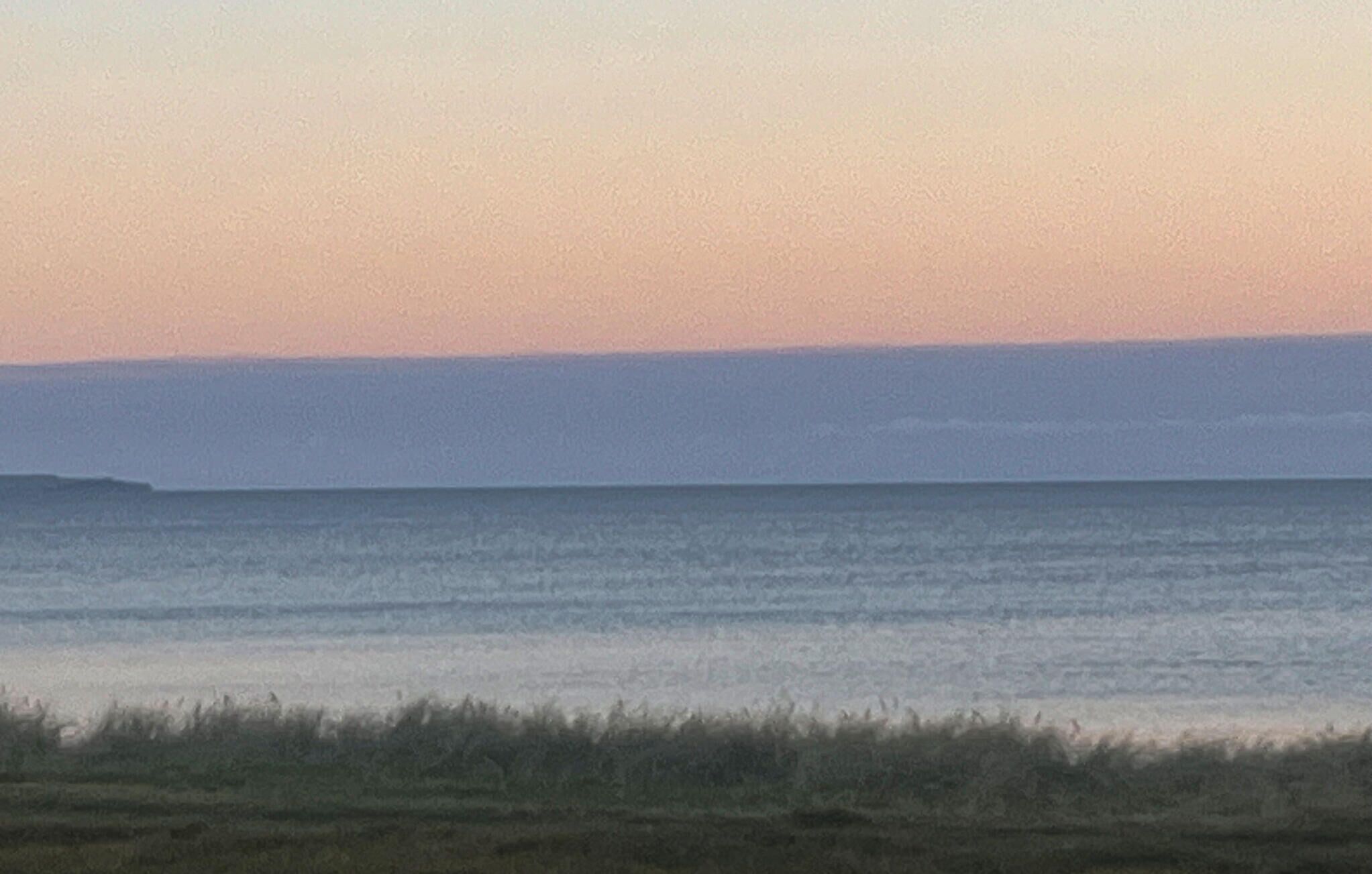 A coastal landscape with a flat horizon and a clear sky.