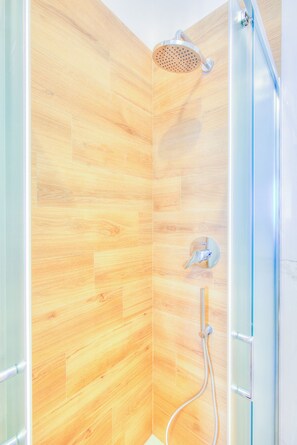 A shower with a wooden panel wall, a glass door, and a handheld showerhead.