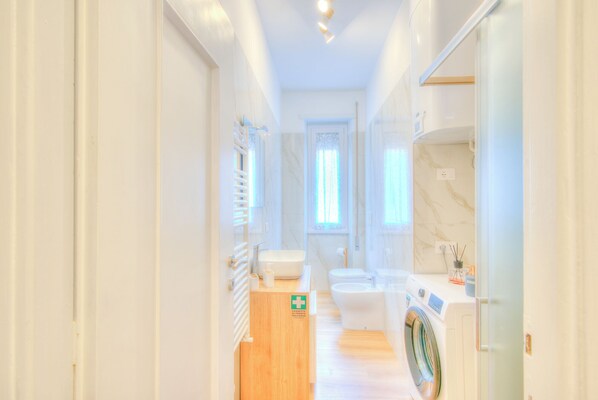 A narrow hallway leading to a bathroom with a toilet, bidet, and washing machine.