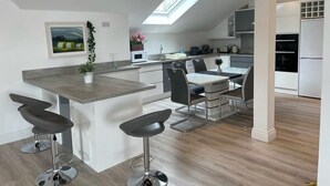 A modern kitchen with a skylight, bar stools, a dining table, and a refrigerator. - Luxury Waterfront Apartment (Cuilmore)