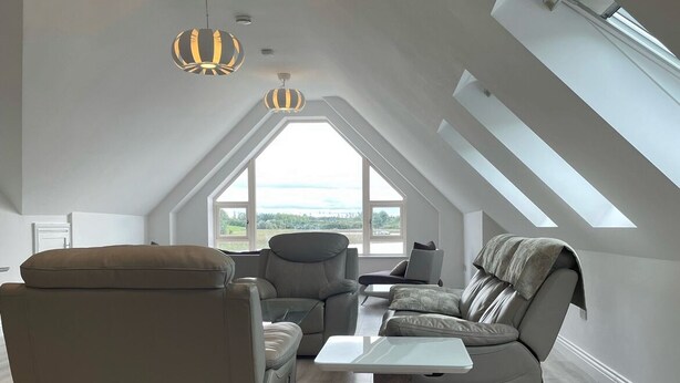 A spacious loft bedroom with a sloped ceiling, large skylights, and a view of the outdoors. - Luxury Waterfront Apartment (Cuilmore)