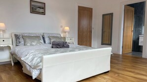 A bedroom with a large bed, two bedside tables with lamps, a wooden floor, and a door leading to another room. - Luxury Waterfront Apartment (Cuilmore)