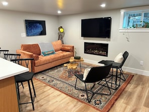 Una sala de estar moderna con un sofá, sillas, un televisor, una chimenea y una alfombra estampada.