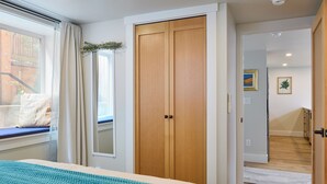 Una camera da letto con un letto, una finestra con tende, un armadio in legno e vista su una scala in legno.