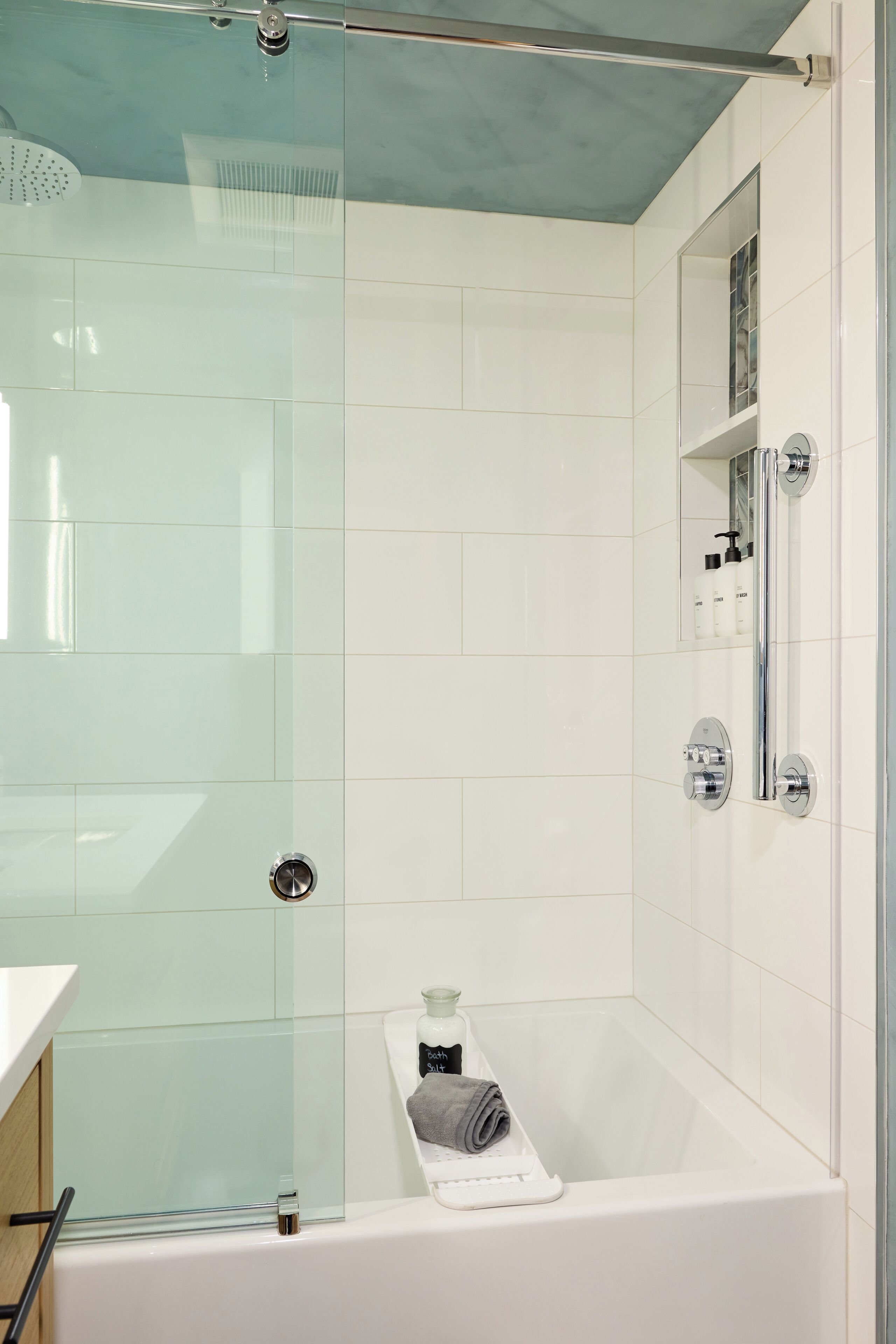 Een moderne badkamer met een douchecabine van glas, een witte badkuip en een ingebouwde plank met toiletartikelen.
