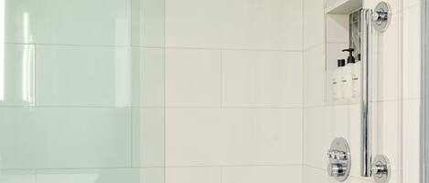 Een moderne badkamer met een douchecabine van glas, een witte badkuip en een ingebouwde plank met toiletartikelen.