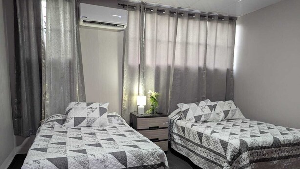 Une chambre d’hôtel avec deux lits, une table de chevet, un appareil de climatisation et une fenêtre avec des rideaux.