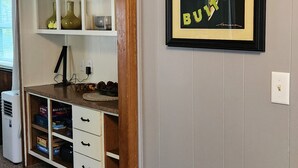 A room with a built-in wooden cabinet with multiple shelves and drawers, a framed poster on the wall, and a carpeted floor.