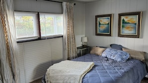 A bedroom with a bed, a nightstand, a lamp, two paintings, and a window with curtains.