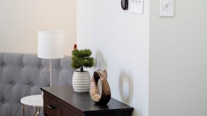 Un salon moderne avec un canapé capitonné, une petite table ronde, un élément décoratif mural, un tableau encadré et une petite plante en pot.