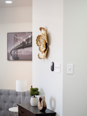 Una sala de estar moderna con un sofá capitonado, una mesita redonda pequeña, un adorno de pared decorativo, un cuadro enmarcado y una planta pequeña en maceta.