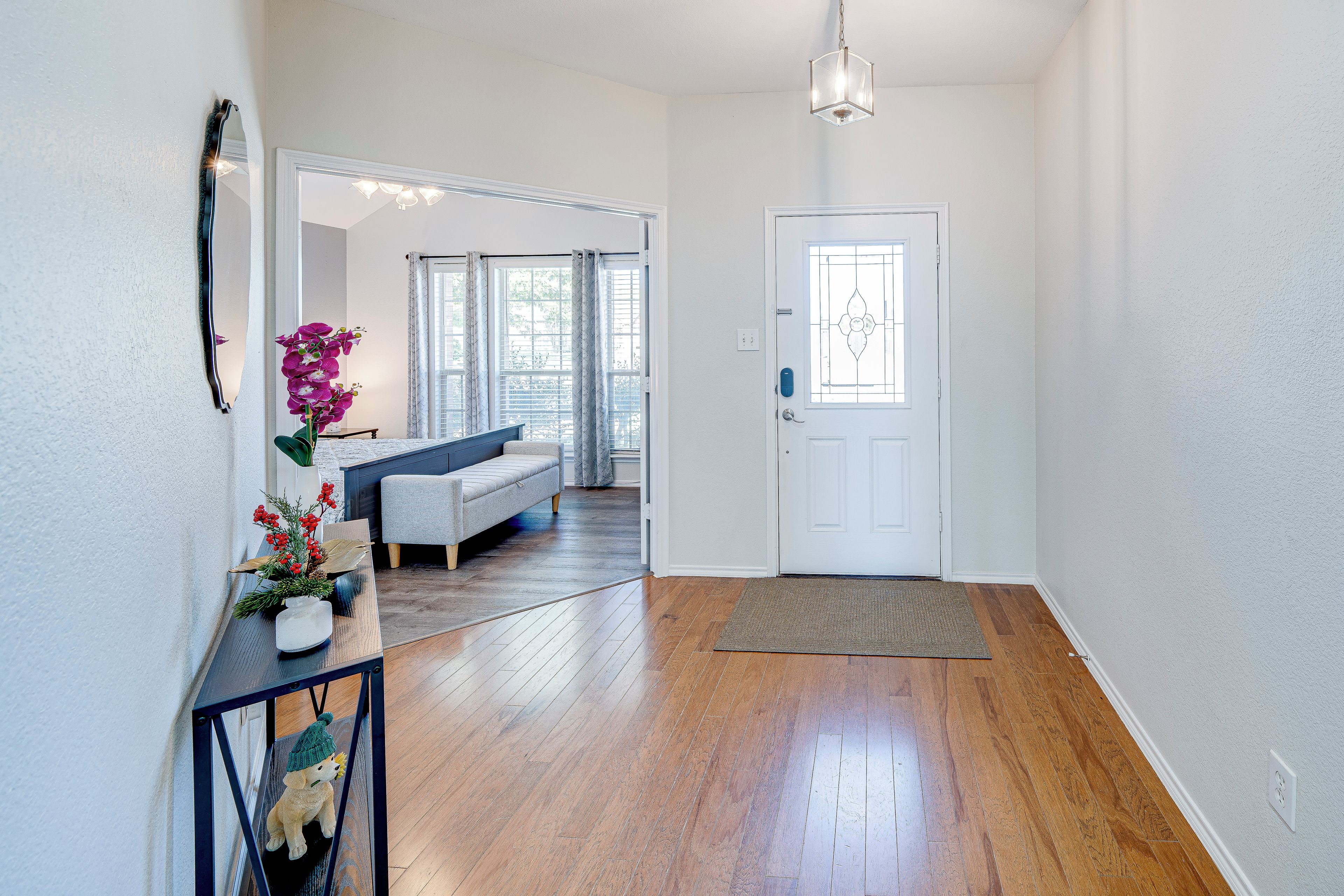 A hallway with a wooden floor, a white door with a glass panel, and a bench in the background.