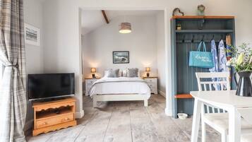 A bedroom with a bed, bedside tables, a TV, a coat rack, and a dining area with a table and chairs.