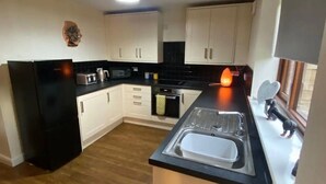 Una cucina compatta con mobili bianchi, un frigorifero nero, un forno a microonde e un lavello.