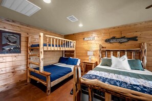 Una habitación tipo cabaña con dos literas, un cabecero de madera, un letrero de bienvenida y una decoración de pared con motivos de peces.