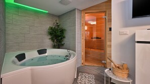 Une salle de bain moderne avec une baignoire sur pieds, une porte en bois donnant accès à un sauna, et une petite table sur laquelle se trouvent un bol en bois et une bouteille.