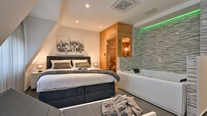 Une chambre à coucher moderne avec un grand lit, une table de chevet, une commode, une baignoire intégrée et un grand miroir.