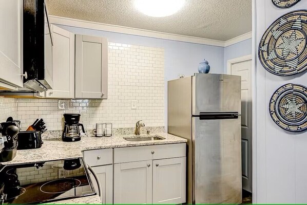 Una cocina con armarios blancos, un refrigerador de acero inoxidable, una cafetera y un lavamanos.