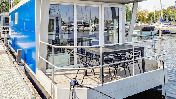 Una terrazza vetrata con tavolo e sedie, affacciata su una marina con barche.