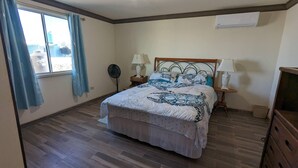 A bedroom with a bed, two bedside tables with lamps, a ceiling fan, and a window with curtains.