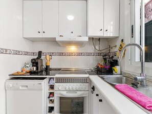A compact kitchen with white cabinets, a built-in oven, a coffee machine, and a sink.