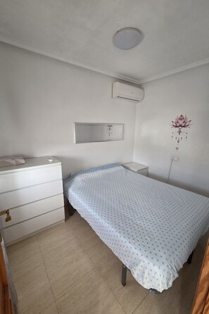 A bedroom with a bed, a dresser, a mirror, and an air conditioning unit.