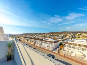 A coastal town with white buildings, a clear sky, and a street with parked cars.