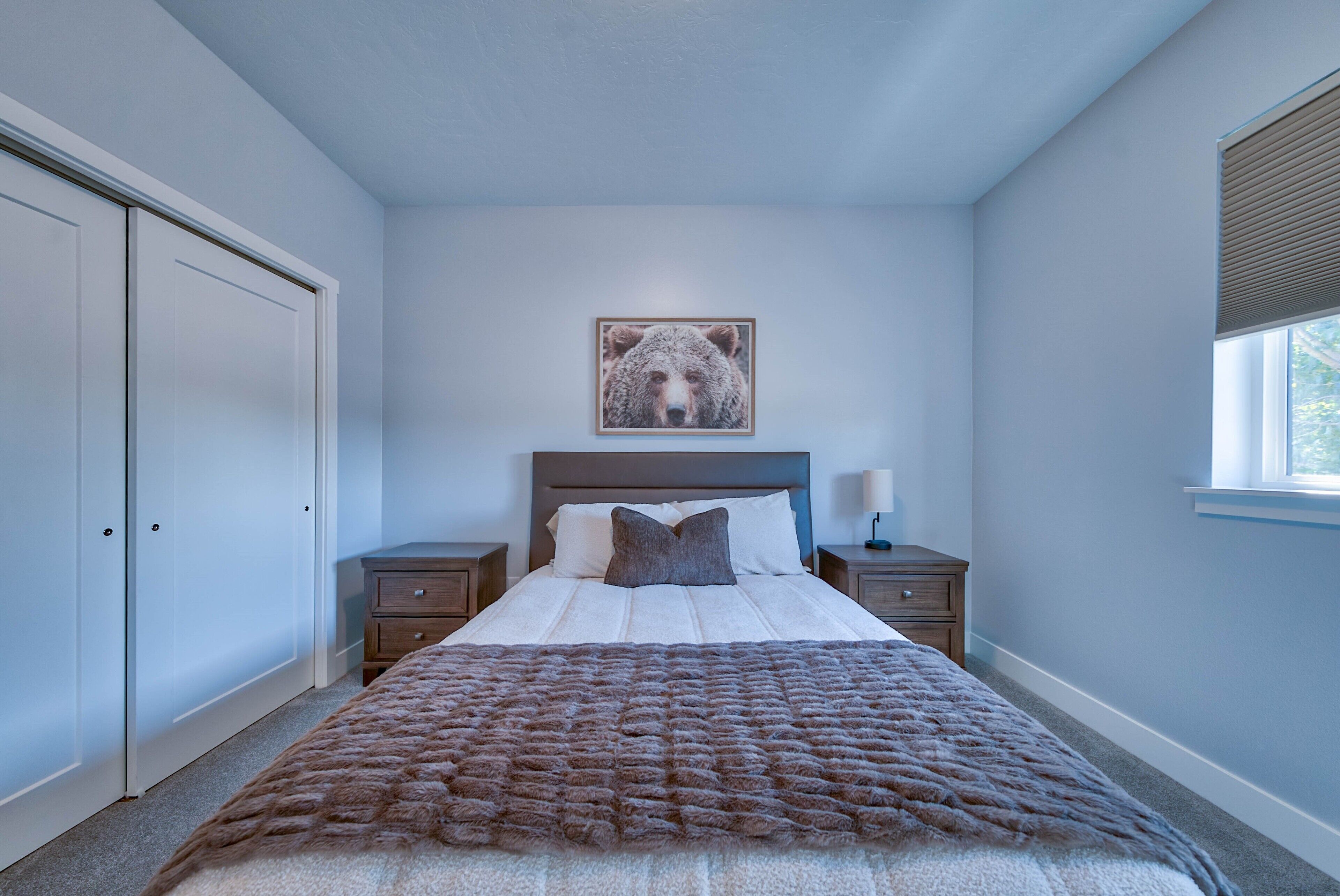 A bedroom with a bed, a nightstand, a dresser, a window, and a wall-mounted picture.
