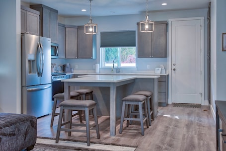 A modern kitchen with a central island, bar stools, stainless steel appliances, and pendant lighting.