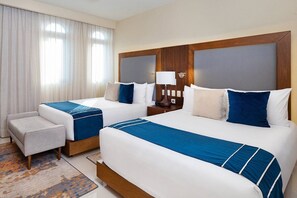 Una habitación de hotel con dos camas, una pequeña zona de estar y una mesita de noche con lámpara.