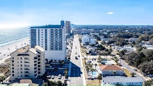 A coastal cityscape with a prominent hotel featuring multiple floors, a parking lot, and a beach in the background. - A Walk From the Beach, 2bed 2bath apartment in 3unit building 1 block from Ocean (North Myrtle Beach)