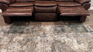 Un canapé en cuir marron, doté d’un repose-pieds et d’un pouf assorti, est placé sur un tapis à motifs.