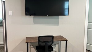 Une pièce équipée d’un téléviseur à écran plat fixé au mur, d’un bureau en bois et d’un fauteuil de bureau noir.